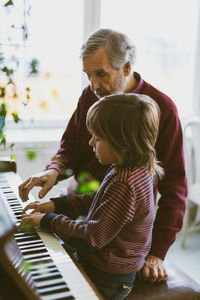 Boy and great grandfather playing piano together at home