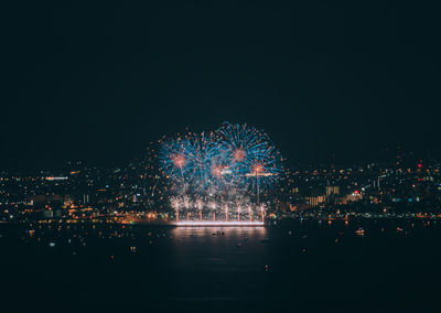 Firework display over illuminated city against sky at night