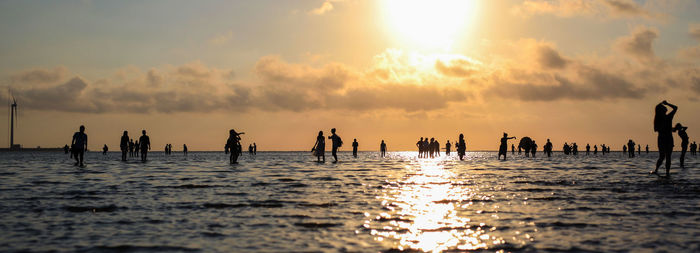 Silhouette people on sea against sky during sunset