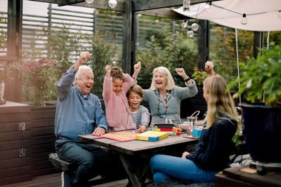 Cheerful family playing board game while sitting at table in backyard