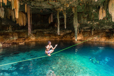 Shirtless man balancing on rope over water in cave