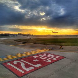 Road sign at airport against sky during sunset