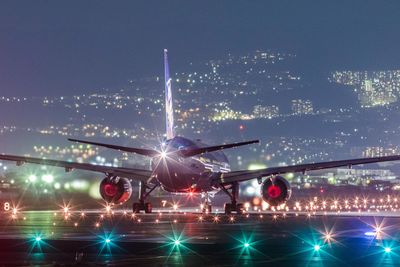 Airplane flying over illuminated airport runway against clear sky at night