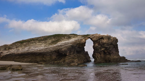 Arch shaped rock formation in sea against sky