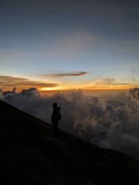 Rear view of man standing on mountain against sky during sunset