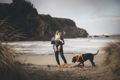 A woman with an infant is playing with a dog on the californian beach