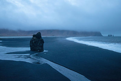 Rear view of woman standing at beach against sky