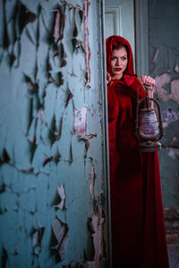 Portrait of young woman standing against red wall