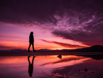 Silhouette man standing in sea against sky during sunset