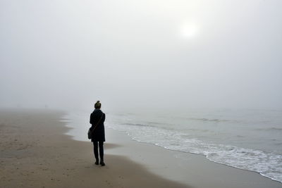 Rear view of woman standing on shore at beach against sky