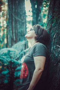 Side view of woman looking at tree trunk