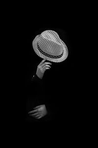 Midsection of woman holding hat against black background
