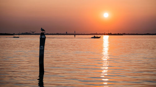 Rear view of woman standing by lake against sky during sunset