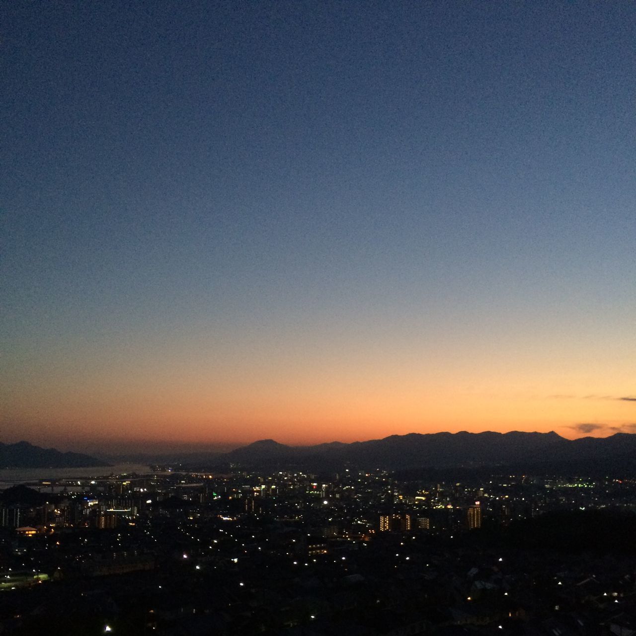 illuminated, copy space, cityscape, night, city, clear sky, scenics, sunset, silhouette, dark, aerial view, dusk, landscape, beauty in nature, building exterior, high angle view, sky, mountain, crowded, blue