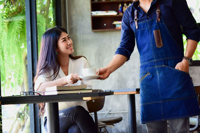 Midsection of waiter serving coffee while woman sitting on table at cafe