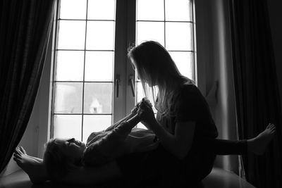 Side view of mother playing with daughter by window at home