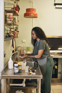 Mature woman washing paintbrushes under faucet in art class