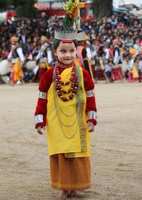 Girl in traditional costume standing against crowd during celebration