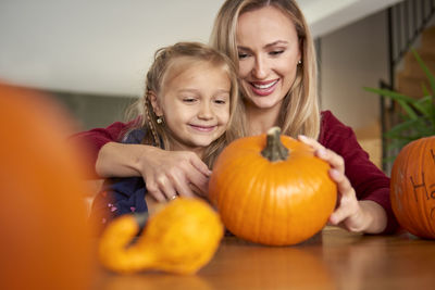 Happy mother and daughter carving pumpkins on table at home