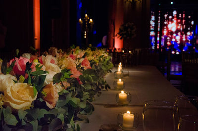 Illuminated candles by multi colored flowers on table