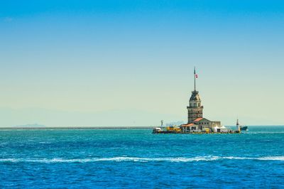 Lighthouse in sea against clear blue sky