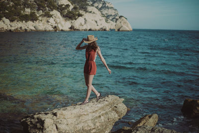 Woman wearing hat standing on rock against sea