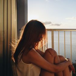 Woman looking away while sitting on railing against sky
