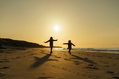 Silhouette people on beach against sky during sunset