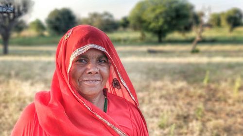 Close-up portrait of mature woman wearing red sari on field