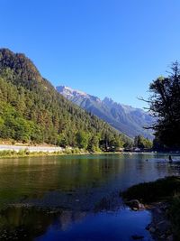 Scenic view of lake and mountains against clear blue sky