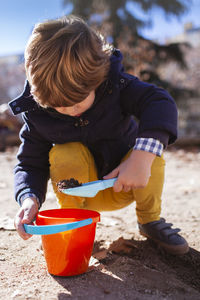 Full length of boy playing with sand pail and shovel while crouching at beach