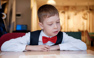 Boy in a white shirt and a red bow tie sits in a cafe and reads the menu.schoolboy in a cafe chooses 