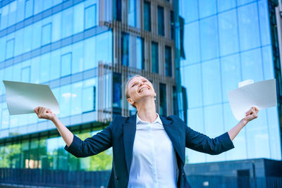 Business woman holding papers in her hands raised up, happy smiling