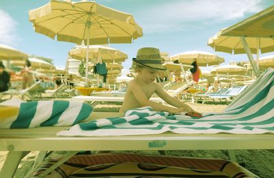 Shirtless boy playing with toy car on lounge chair at beach