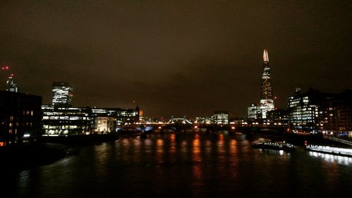 Illuminated buildings by river against sky at night