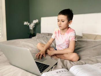 Cute boy using laptop while sitting on bed at home