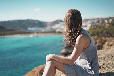 Side view of young woman sitting against sea