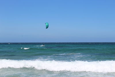 Scenic view of sea against clear blue sky with person kiteboarding in background