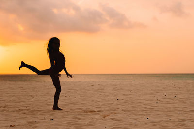 Silhouette woman on beach against sky during sunset