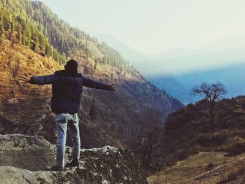 Rear view of man with arms outstretched standing on mountain against sky