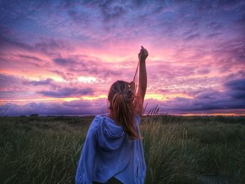 Rear view of woman with arms raised standing against sky during sunset