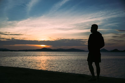 Rear view of silhouette man standing at beach during sunset