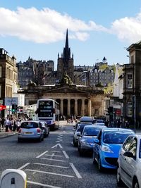 Cars on road by buildings against sky in city