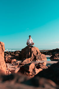 Man sitting on rock against blue sky