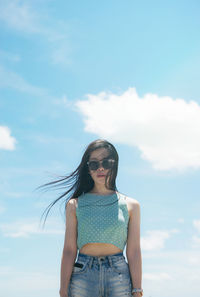 Young woman wearing sunglasses standing against sky