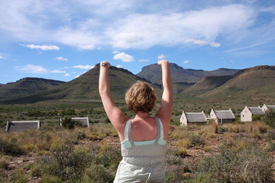 Rear view of woman with arms raised against sky