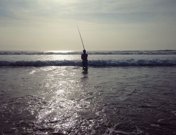 Silhouette man fishing in sea against sky