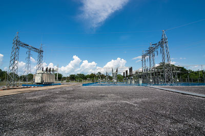 Road by electricity pylon against blue sky