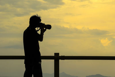 Silhouette man photographing against sky during sunset