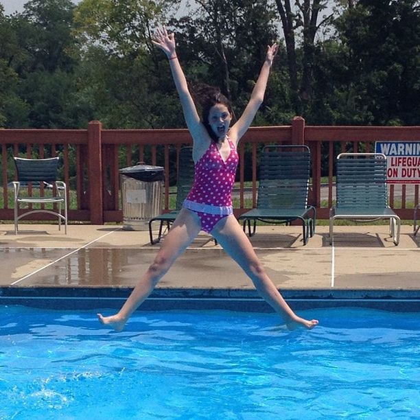 full length, lifestyles, leisure activity, young adult, person, water, casual clothing, enjoyment, young women, front view, jumping, swimming pool, tree, fun, dress, happiness, arms outstretched, blue